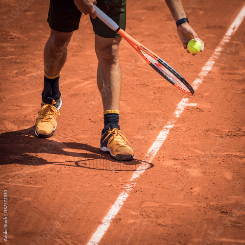 Tennis player with a ball and a rackey on a clay court at Rolland Garros