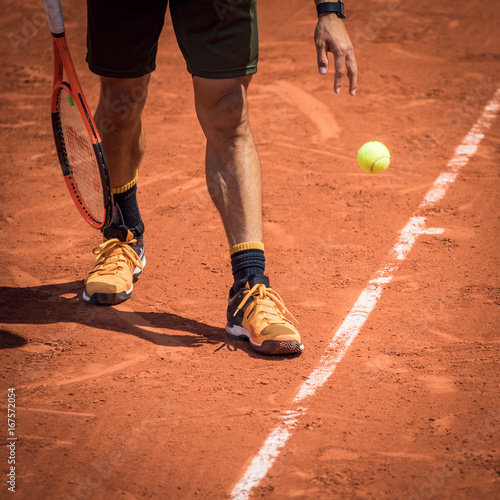 Tennis player with a ball and a rackey on a clay court at Rolland Garros