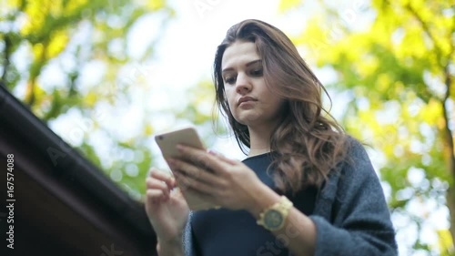 Portrait view below attractive woman holding using smart phone looking screen watch calm walking tapping touching beautiful brunette girl fashionable summer sky blurred trees background nature outside photo