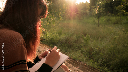 Young woman with pen writing on notebook at nature.