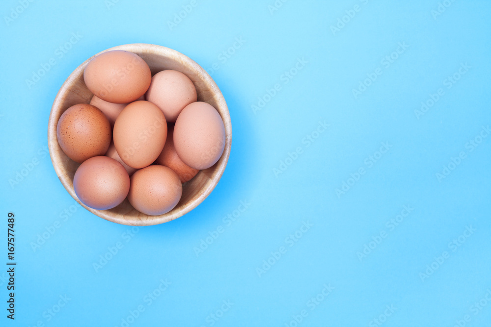 Chicken egg in wood bowl on blue background with space for copy .
