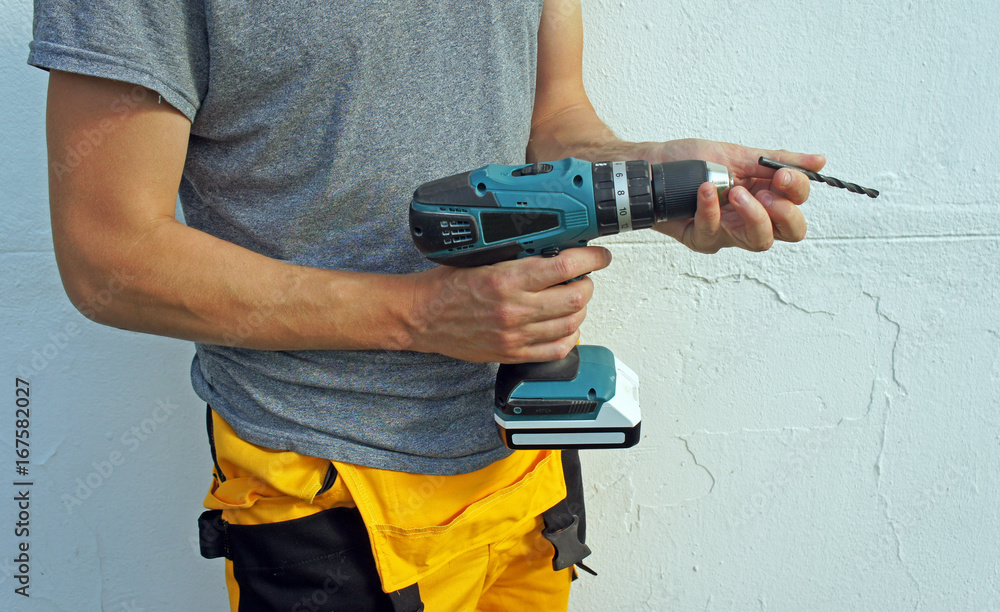 Electric screwdriver in hand of worker, drill replacement, white wall background Electric screwdriver in hand of worker, drill replacement, white wall background