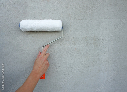 Paint roller in hand of worker, grey wall background