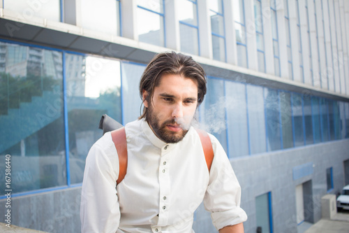 handsome guy with beard smocking cigarette on urban background with blue and gray glass  