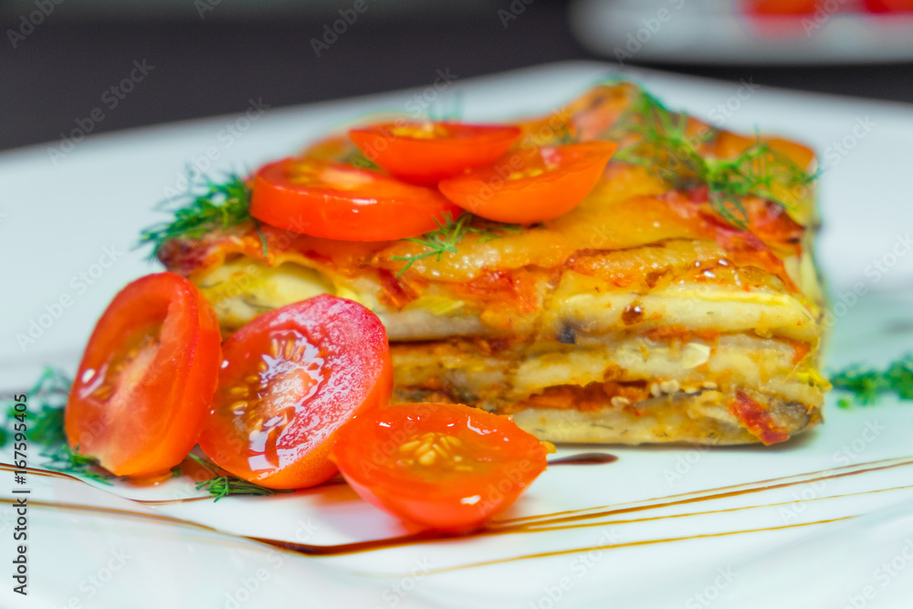 Lasagna with tomatoes on a white plate