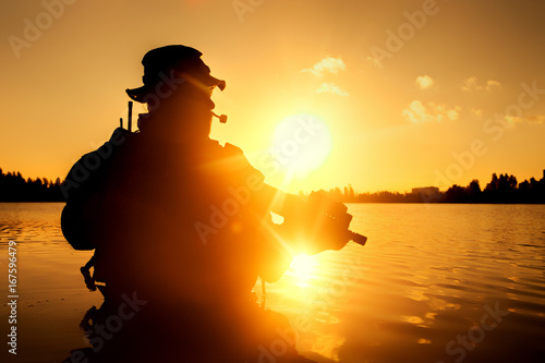 Silhouette of special forces with rifle in action during river raid in the jungle waist deep in the water. Proflie side view  half length