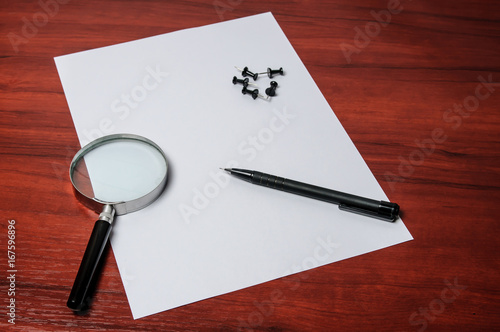 A blank sheet of paper with a pencil, magnifying glass and pushpins