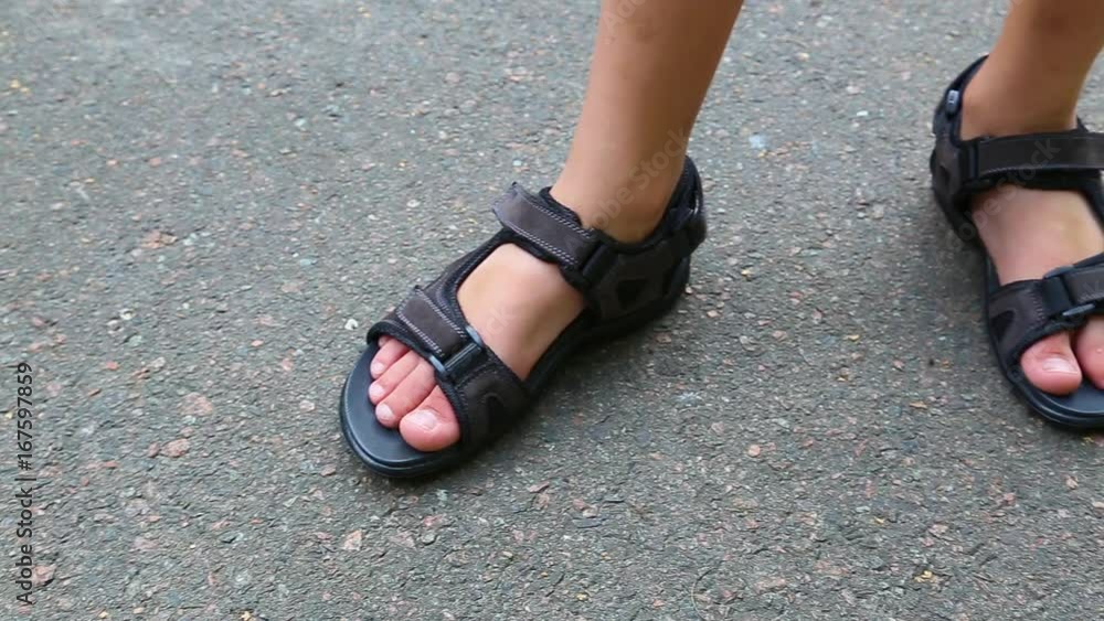 Closeup top view of feet of white child wearing brown leather sandals with black rubber sole isolated on grey urban pavement. Real time full hd video footage. Closeup top view of feet of white child wearing brown leather sandals with black rubber sole isolated on grey urban pavement. Real time full hd video footage.