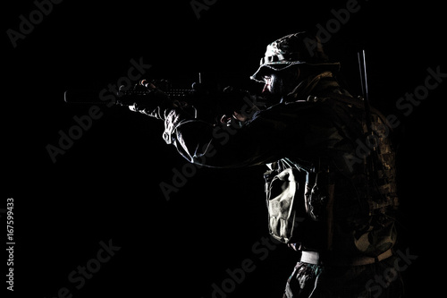 Bearded Special forces United States in Camouflage Uniforms studio shot half length black background, backlit. He is shooting killing enemy, pointing the rifle