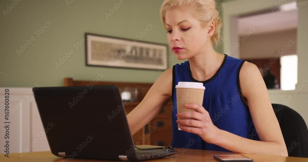 Caucasian businesswoman working on laptop at desk inside home, answering text message on cell phone. Self-employed female responding to text on smart phone at table in dining room. 4k Caucasian businesswoman working on laptop at desk inside home, answering text message on cell phone. Self-employed female responding to text on smart phone at table in dining room. 4k