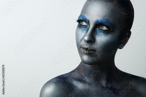 Portrait of a close-up girl. Creative make up, face art, body art. Blue paint on the face. Look to the side