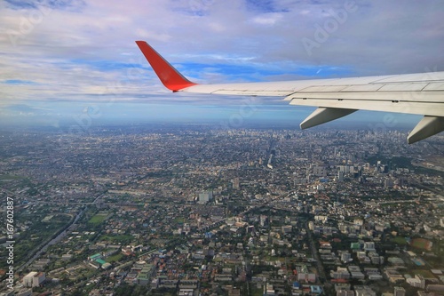 Aerial view of Bangkok  Thailand with building in big city  blue sky  white cloud and airplane s wing. View from airplane s window. Soft focus.