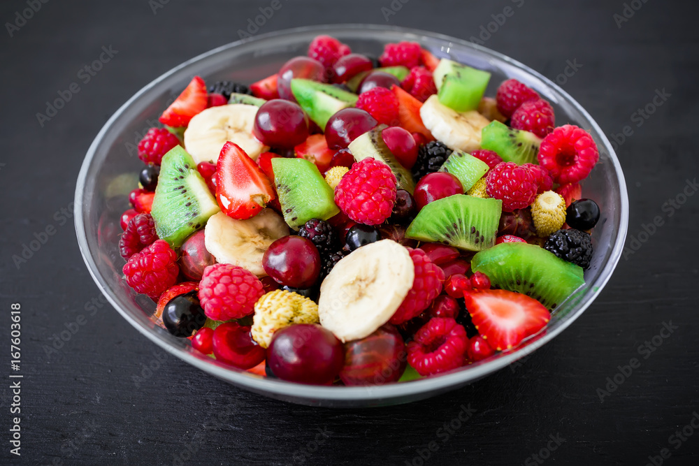 Fresh fruit salad in glass plate on dark background. Flat lay, top view Fresh fruit salad in glass plate on dark background. Flat lay, top view