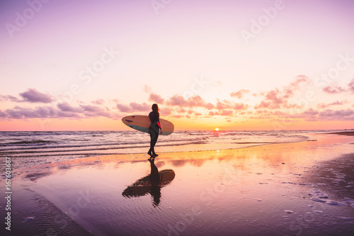 Photography Surf girl with surfboard on a beach at colorful sunset