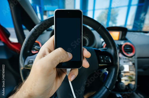 The driver holds a smartphone in his hand with an application showing the road or navigator. Blank screen.