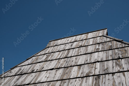 Old shake roof with weathered wooden planks and deep blue sky above
