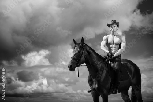 Macho man handsome cowboy and horse on the background of sky and water.