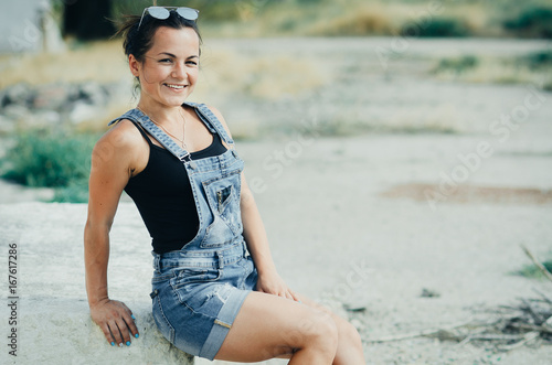 Girl in denim overalls sits on a concrete slab