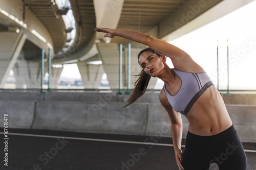 Young sportswoman doing stretching exercise under a bridge