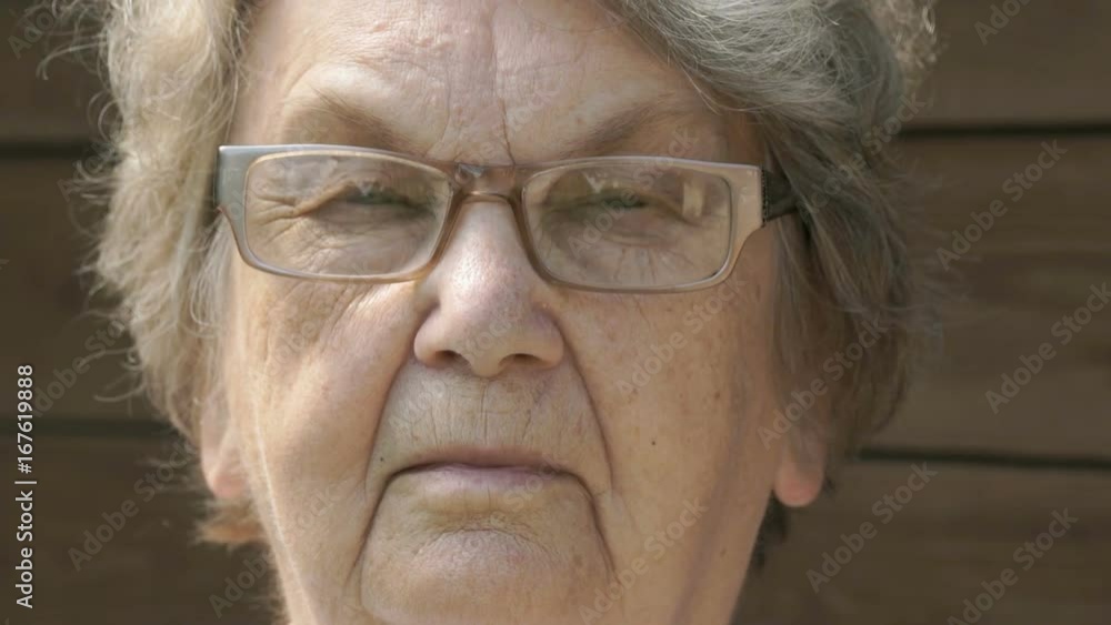 Portrait of serious mature old gramma aged 80s in glasses outdoors in the background of wooden boards. Slow Motion Portrait of serious mature old gramma aged 80s in glasses outdoors in the background of wooden boards. Slow Motion