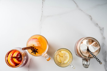 Selection of various autumn traditional drinks: hot chocolate with marshmallow, tea with lemon and ginger, white pumpkin spicy sangria, mulled wine. On white marble table, copy space, top view