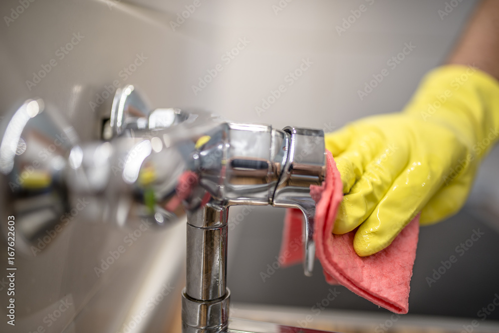 Young handsome man wiping faucet in kitchen