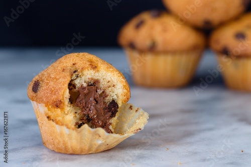 Small and half finished vanilla flavour muffin on marble surface. Several more muffins visible in background
