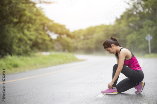young woman runner tying shoelace on country road © FAMILY STOCK