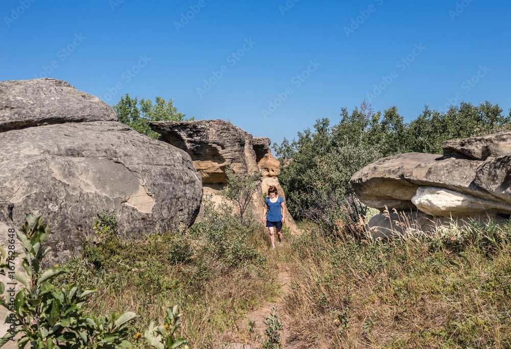 Naklejka premium horizontal image of a caucasian woman on vacation walking among big natural sandstone rock formations on a beautiful summer afternoon.
