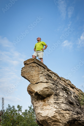 vertical image of a caucasian man on vacation standing at the tip of a tall sandstone rock formation  on a beautiful summer morning.