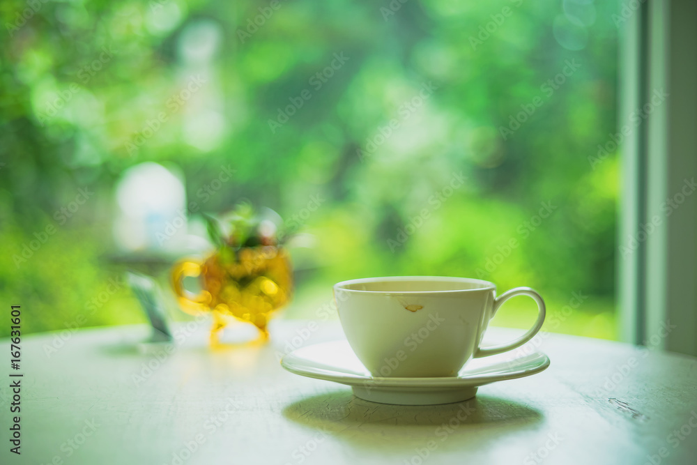 White cup of coffee on the table with morning sunlight and nature background