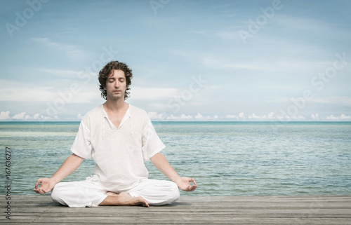 Young man enjoying meditation in Lotus position on the beach.