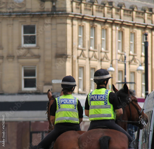 Two Female Police Officers on Horseback Patrol in a City.