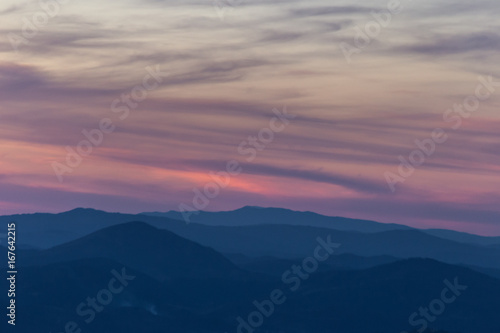 Beautiful dusk over some mountains with blue, purple and red tones in the sky, clouds and hills