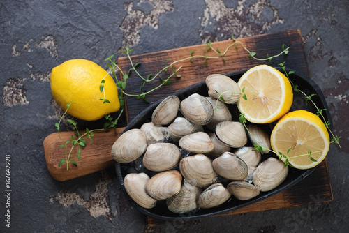 Metal plate with raw fresh vongole clams on a wooden chopping board, brown stone background, flat-lay