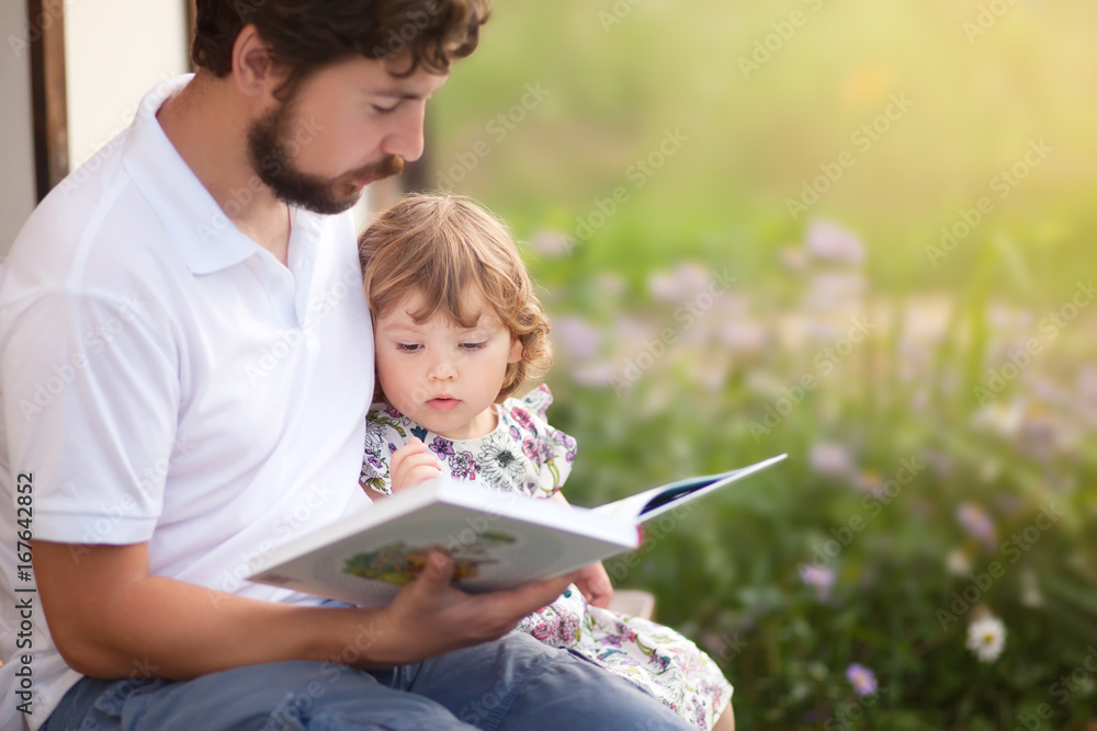 Father reading to his toddler kid, outdoor