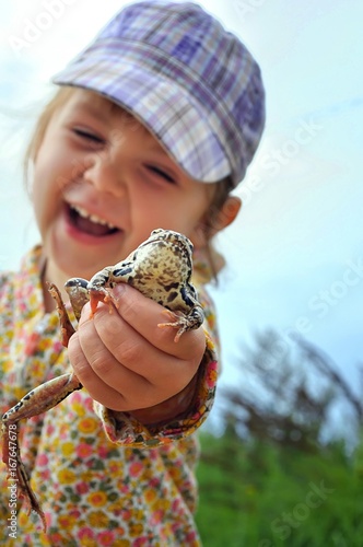A cute young child girl holding a frog toad in hands and laughing