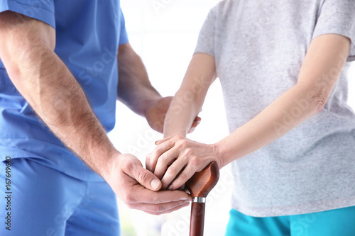 Elderly woman and young man holding hands on walking stick, closeup. Physiotherapy concept