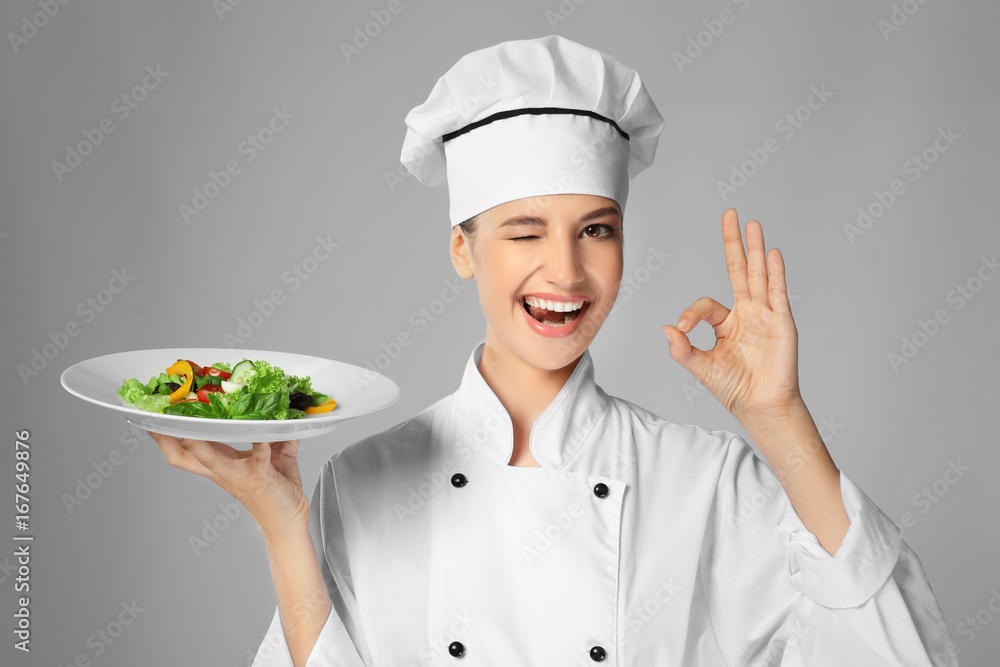 Young female chef holding plate with salad on light background Young female chef holding plate with salad on light background