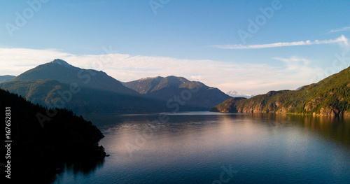 Aerial shot of ocean bay or lake with mountains while sunset