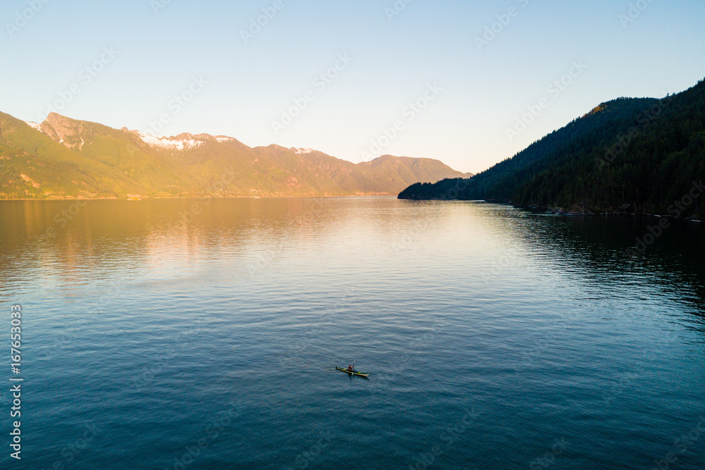 Aerial shot of kayaker on lake with mountains while  sunset