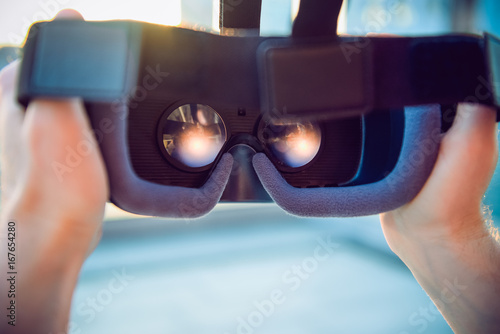 VR Goggles in male hands. Man ready to wear virtual reality goggles. The vr headset design is generic and no logos. Backward light, selective focus, close up. Sunset city landscape.