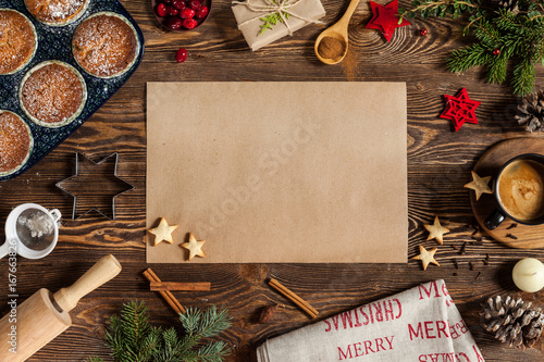 Christmass composition with sweets, cinnamon, and empty piece of paper on center. Branches of furry spruce, cup of coffee, red christmas tree toys on a wooden background.