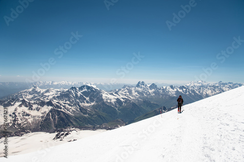 Mountaineer in the mountains strolls along the snow slope against the background of snow-capped peaks