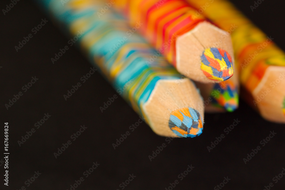 Obraz premium Four multicolored pencils stacked one on three on a plain black background.