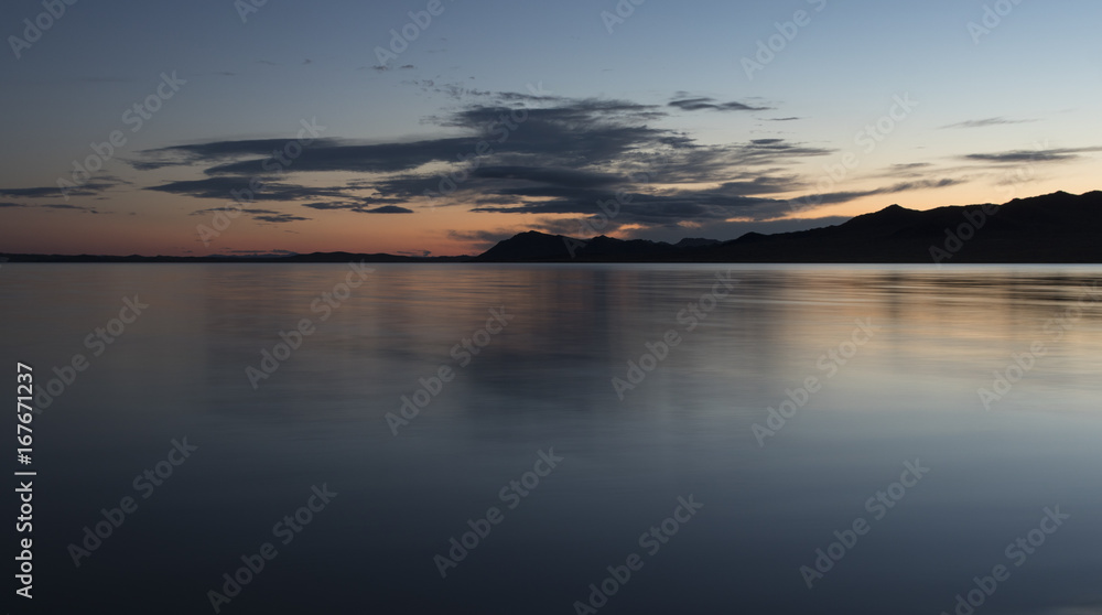 A beautiful lake in Mongolia late in the evening. Blue and orange clouds against the blue sky are reflected in the mirror surface of the lake. Travel photo. Without people.