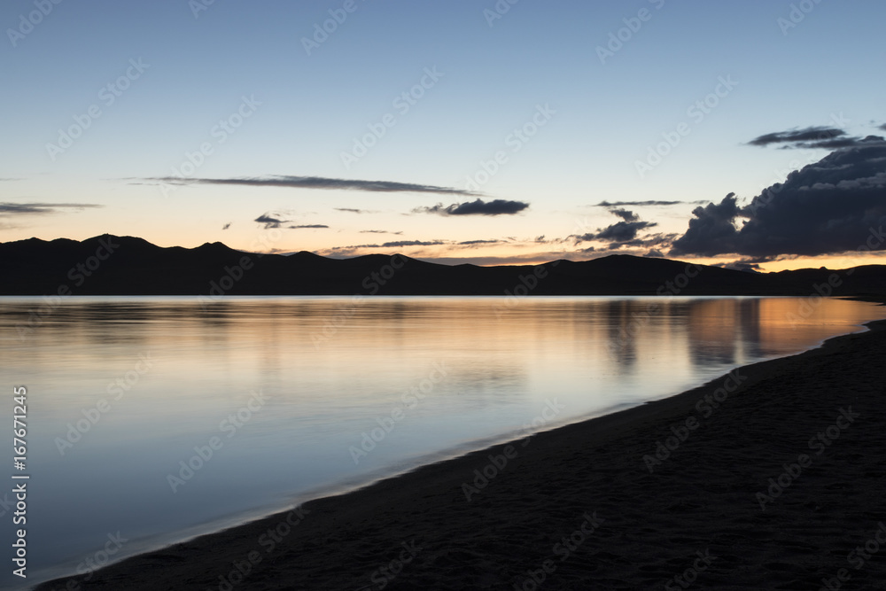 A beautiful lake in Mongolia late in the evening. Blue and orange clouds against the blue sky are reflected in the mirror surface of the lake. Travel photo. Without people.