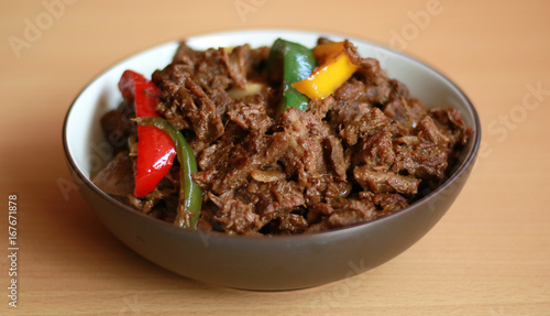 Black pepper beef in bowl with wood background.