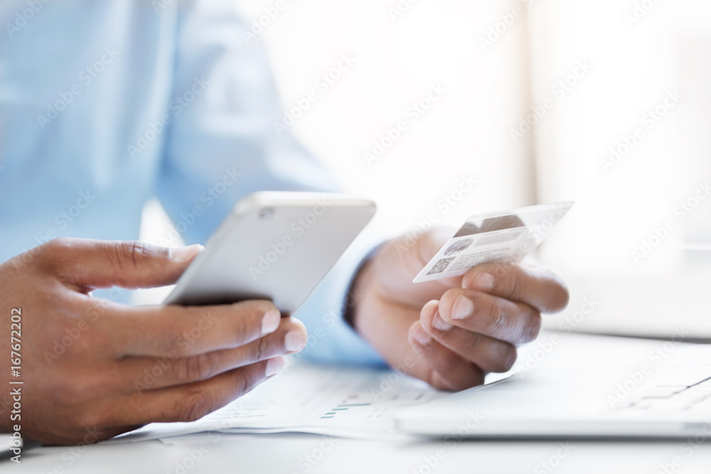 Cropped shot of businessman holding modern cell phone and credit card in hands, making transaction using mobile bank application. Businessman making orders online. People, technology and business Cropped shot of businessman holding modern cell phone and credit card in hands, making transaction using mobile bank application. Businessman making orders online. People, technology and business