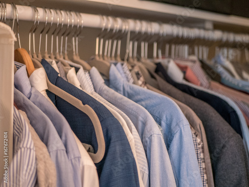 Men's shirts in different colors on hangers in wardrobe.